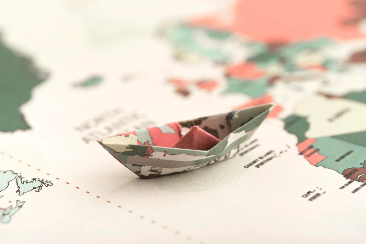 An intricately folded paper boat rests on a world map, representing a journey across continents.