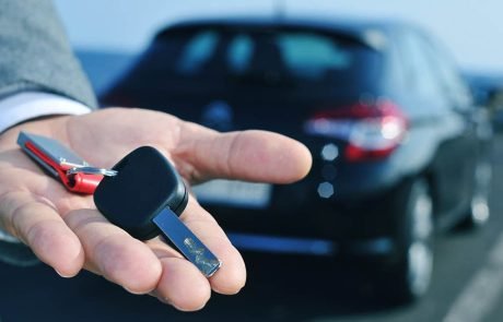 A man holding a car key in front of a sleek car, ready to embark on a journey.